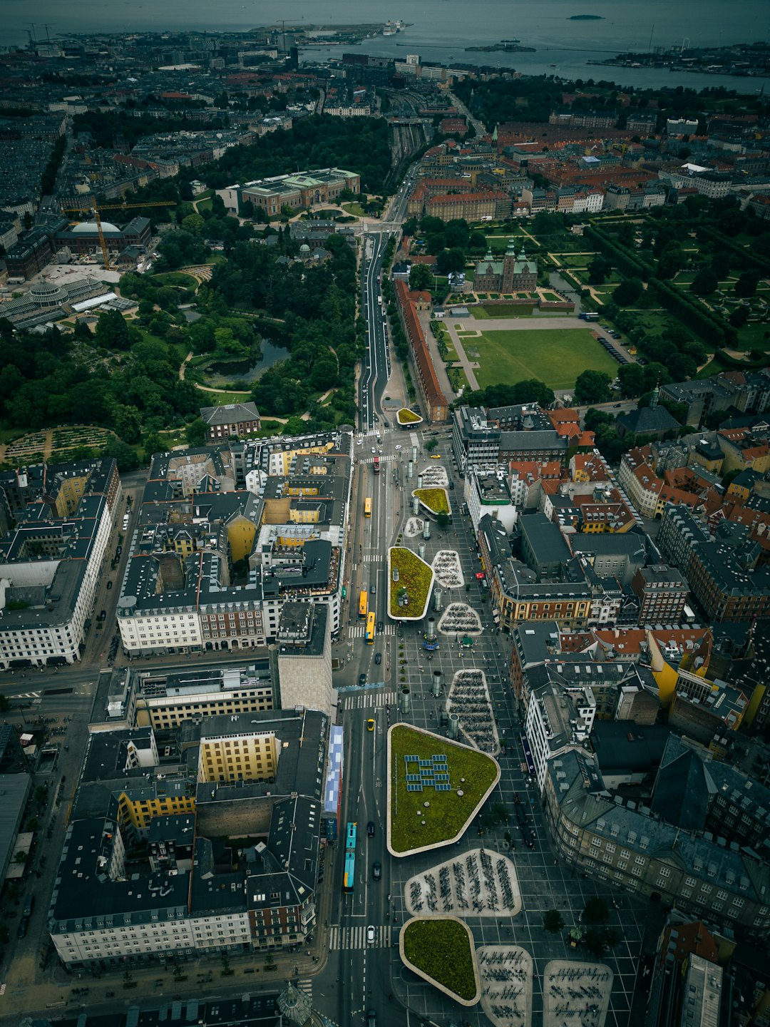 Vista aerea di una strada cittadina con parchi, edifici, auto e autobus.