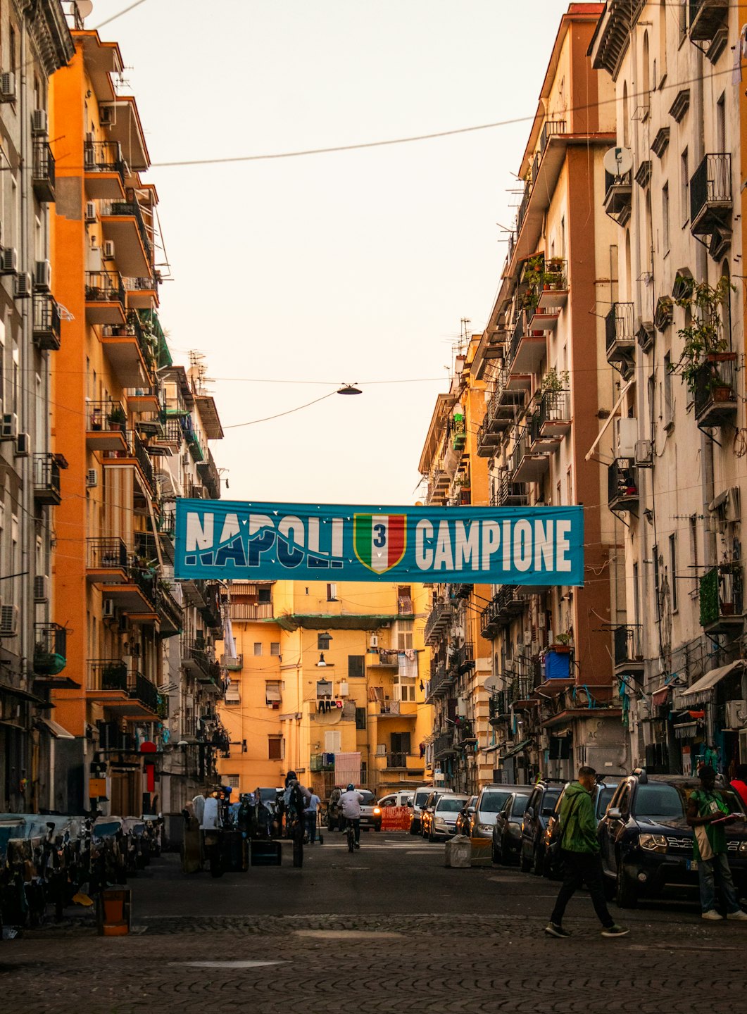 Uno striscione per lo scudetto del Napoli campeggia sopra una strada cittadina trafficata.