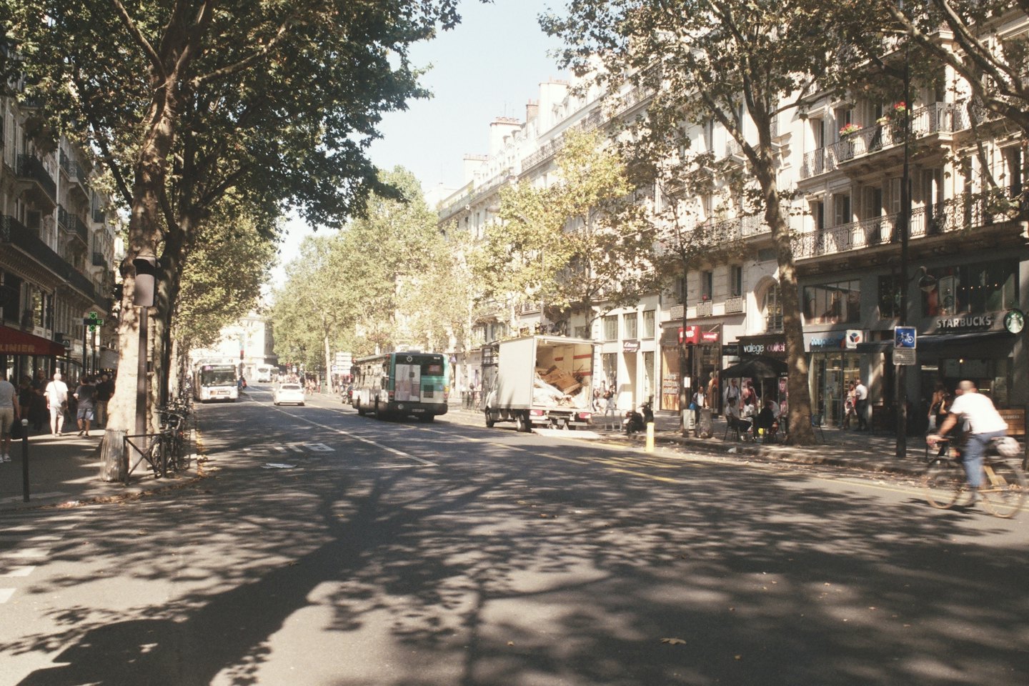 Strada europea soleggiata con pedoni e traffico.
